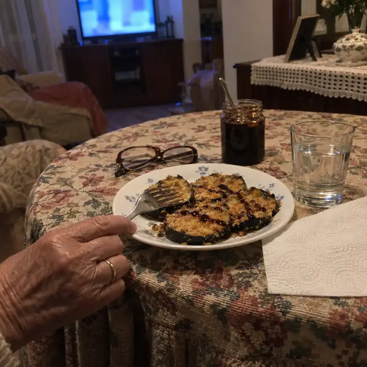 Plato de berenjenas crujientes con miel de caña en una mesa camilla, con unas gafas de leer al lado